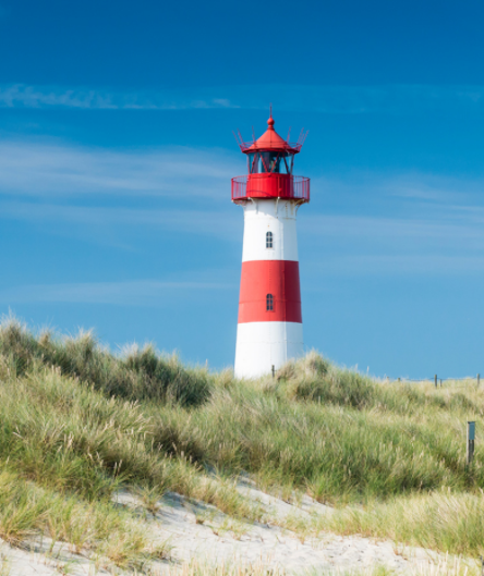 Ein rot-weiß gestreifter Leuchtturm mit roter Laterne steht hinter einer mit Dünengras bewachsenen Sanddüne